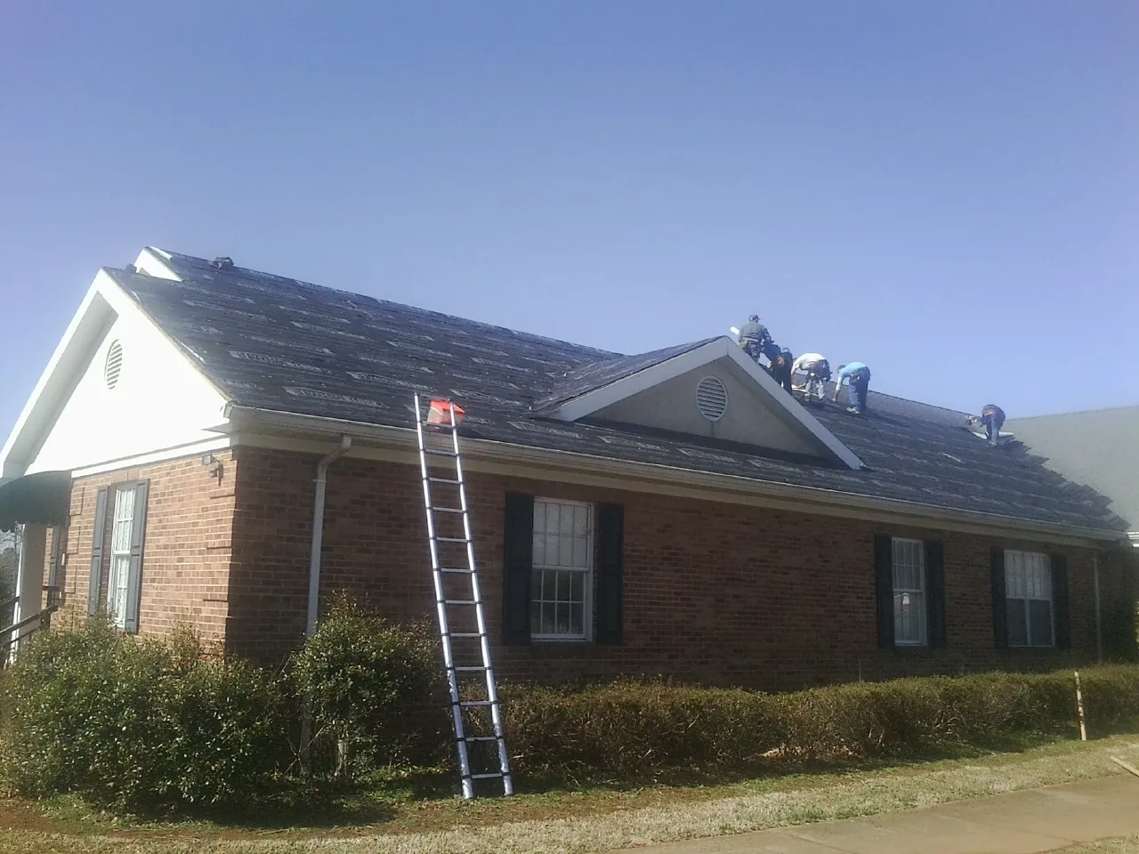Crew tearing shingles off a brick ranch roof with a ladder set — Emergency Roof Repair work by our crew in Puyallup