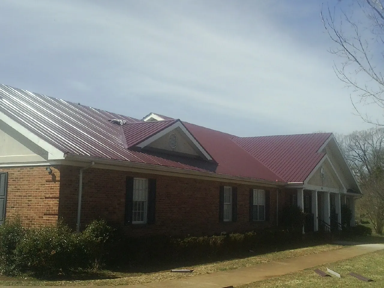 Red metal roof with gabled entries on a long brick building, from a Hail Damage Roof Repair job in Puyallup