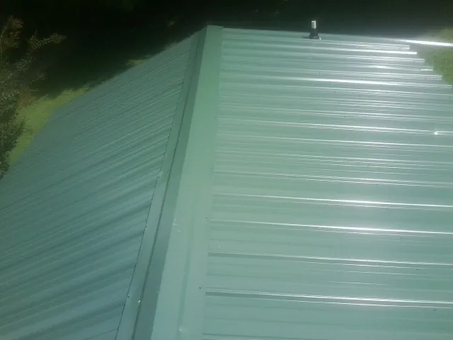 New green metal panels meeting at the ridge of a roof — Flat Roof Repair work by our crew in Puyallup