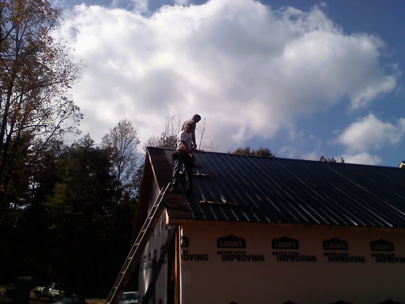 Roofer fastening dark metal panels high against a cloudy sky, from a Roof Inspection job in Puyallup