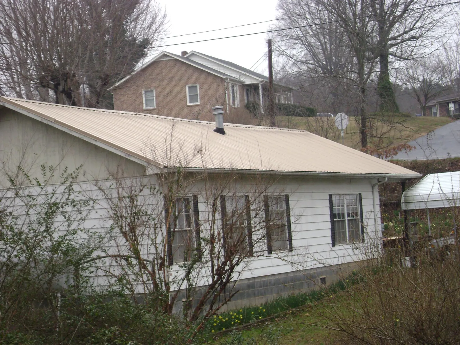 Tan metal roof on a white sided house set into a hillside — Commercial Roofing by Roofing Brothers in Puyallup
